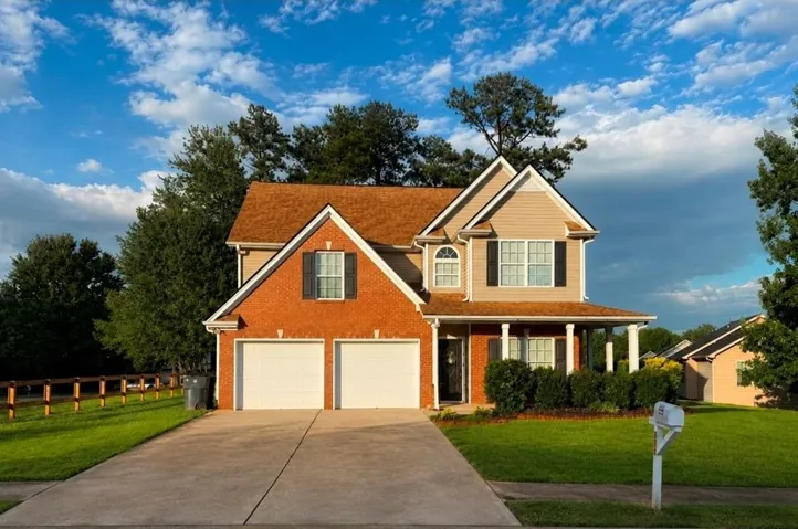 Brick and siding exterior featuring a two-car garage, covered front porch with white columns, and a concrete driveway