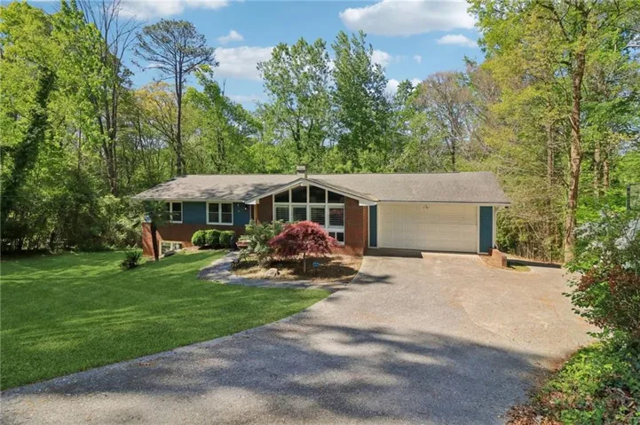 The property features a brick and siding exterior, a driveway, a two-car garage, and a well-maintained lawn with mature trees