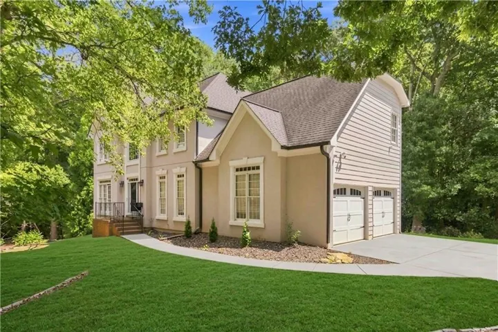 Stucco and siding exterior with a two-car garage, mature trees, and a concrete driveway