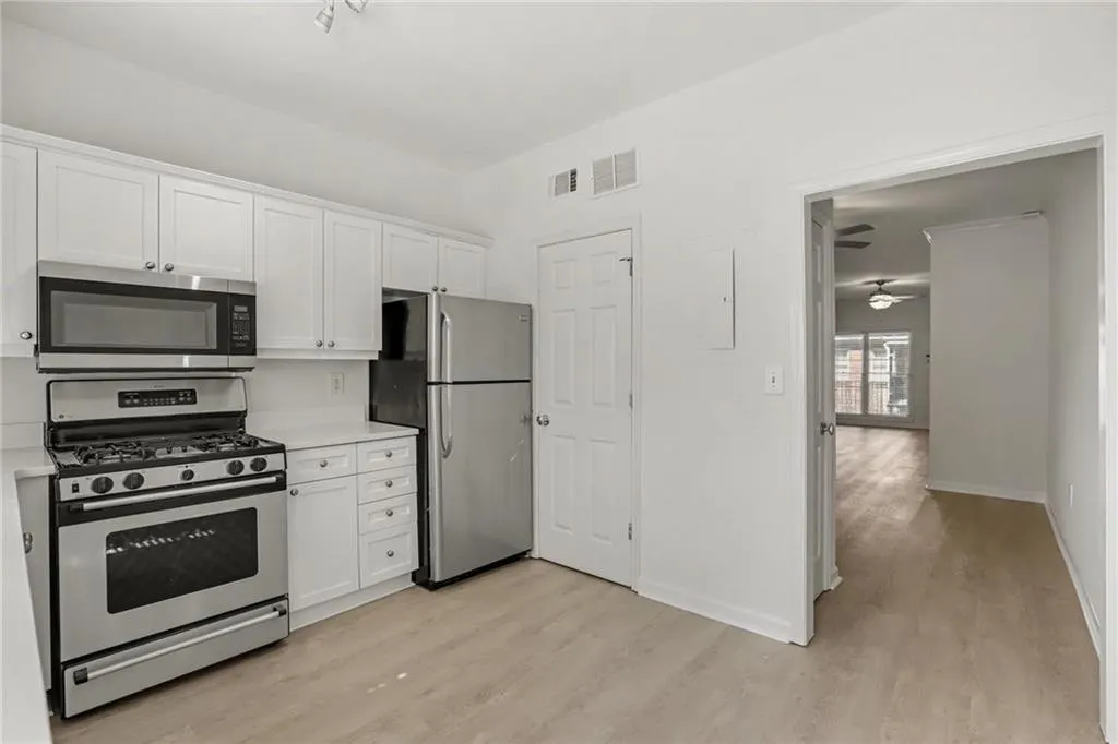 Kitchen featuring stainless steel appliances, white cabinetry, light-toned wood-finish flooring, and white countertops