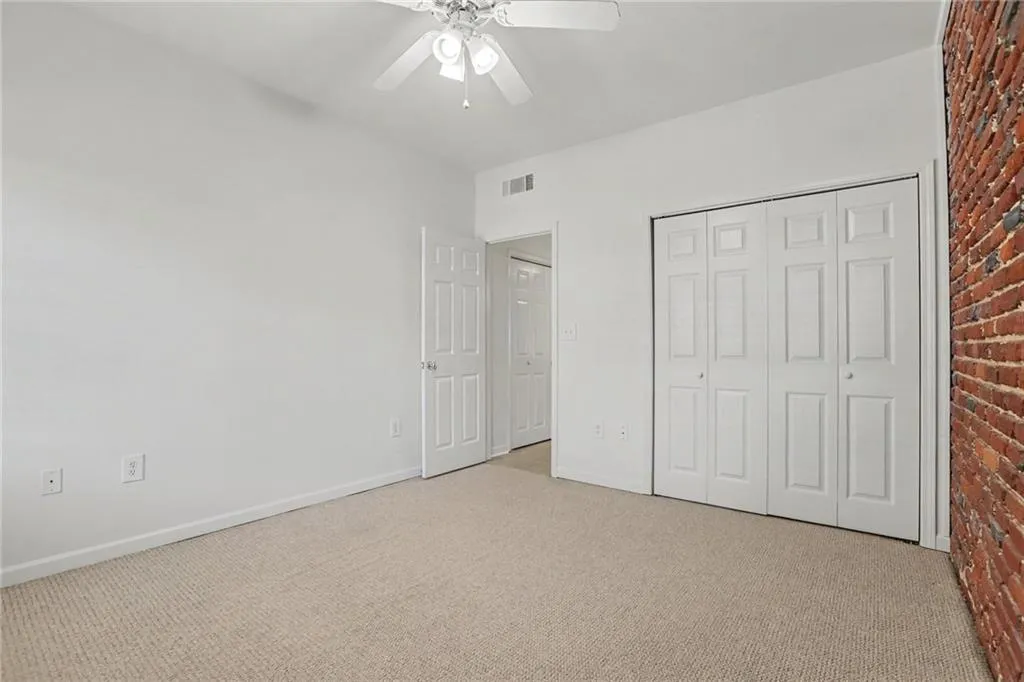 Carpeted flooring, exposed brick accent wall, bi-fold closet doors, white ceiling fan with light, and white paneled doors