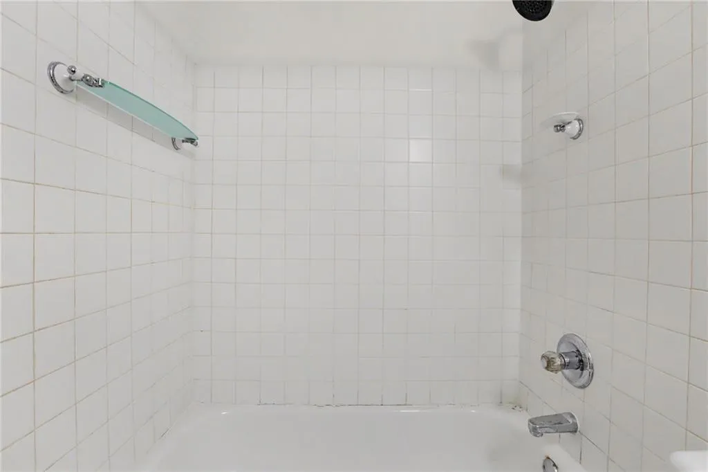 Bathtub with white tiled surround, chrome fixtures, and a glass shower shelf