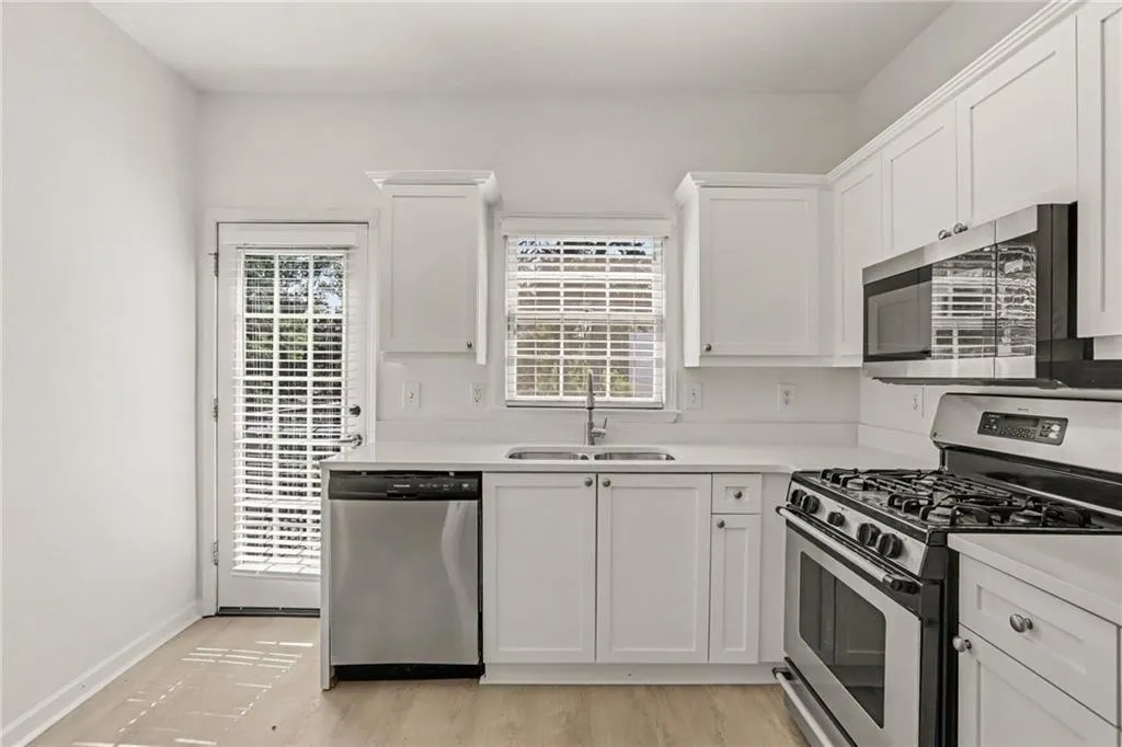 Kitchen featuring white cabinetry, stainless steel appliances, a double basin sink, and wood-finish flooring