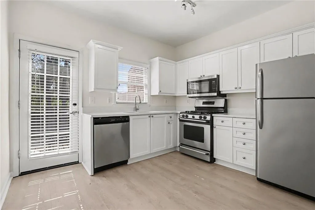 Kitchen featuring white cabinetry, stainless steel appliances, light-toned countertops, wood-finish flooring, and a glass-paned door