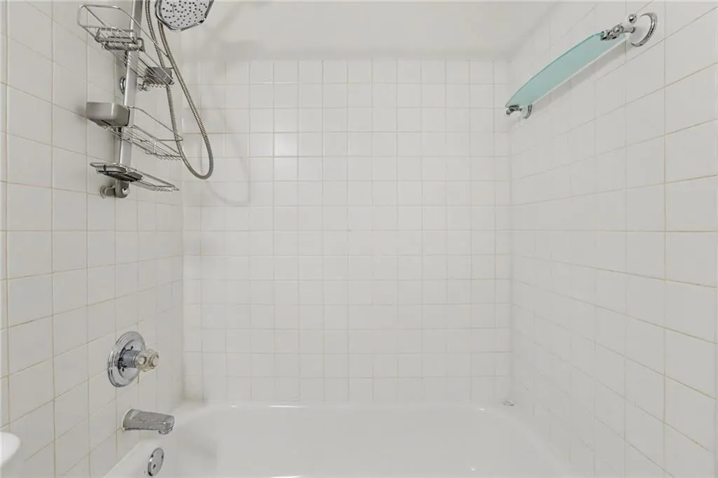Bathtub with white tile surround, chrome fixtures, and glass shelf
