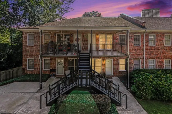 Brick exterior with multiple entryways, upper-level balcony with black railing, and ground-level patio