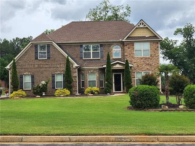 Two-story brick and stone facade residence featuring a prominent front entrance, multiple windows with dark shutters, and a gabled roofline