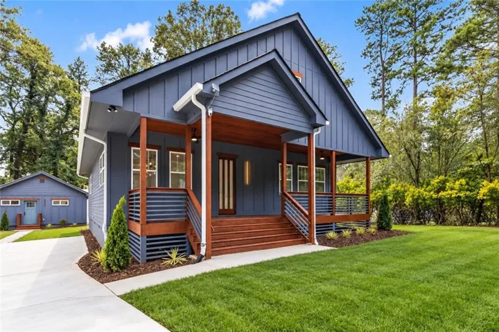 Exterior featuring blue vertical siding, a wood-finish porch with horizontal railings, a concrete driveway, and a detached garage with an accent door