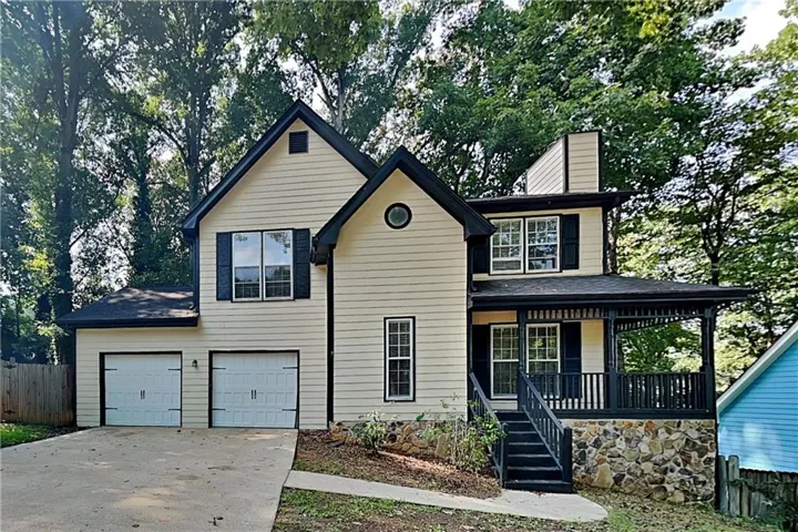 Charming two-story colonial featuring cream-colored vinyl siding with black architectural accents, a covered front porch with black railings, and a peaked roofline with dormer windows