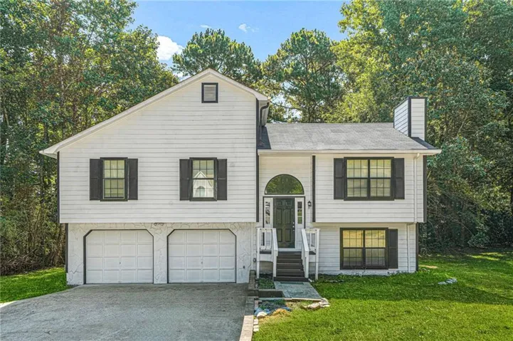Split-level residence featuring white siding, a two-car garage, and a prominent arched transom window above the entry