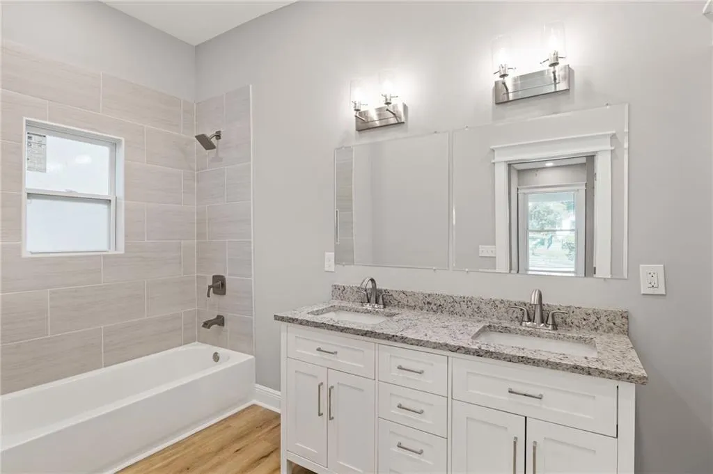 Bathroom featuring double vanity, shower / washtub combination, and wood finished floors