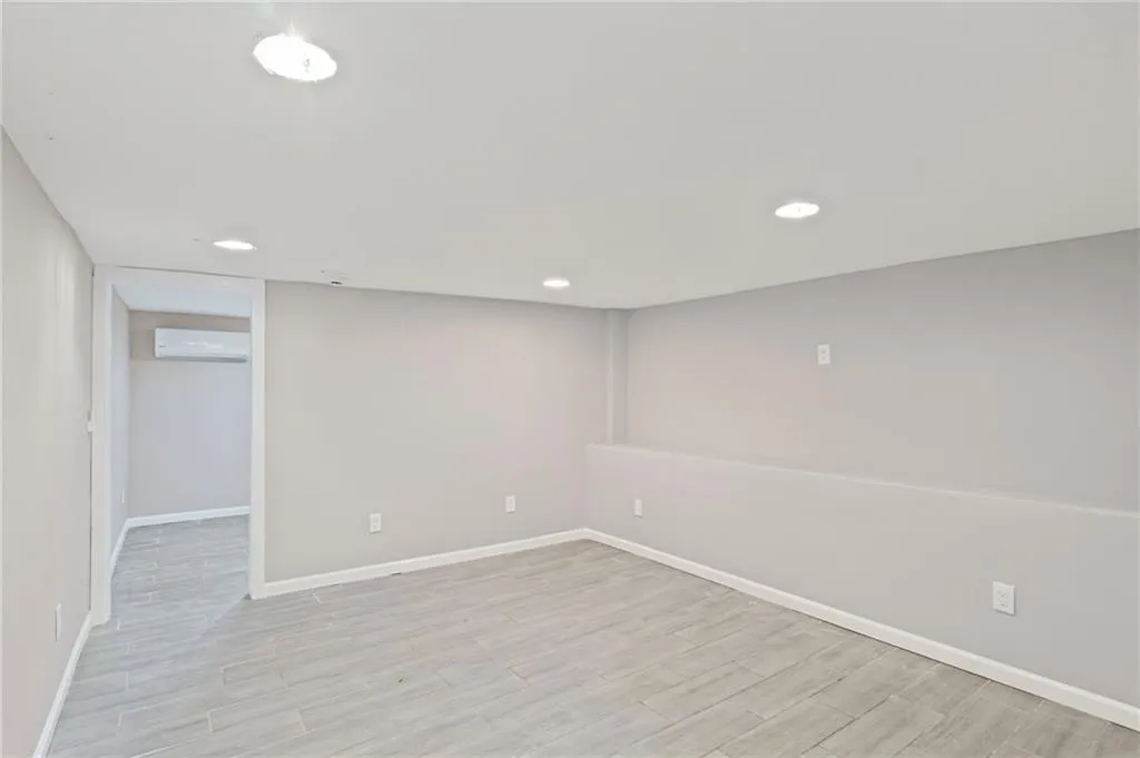 Finished below grade area featuring an AC wall unit, light wood-style flooring, and recessed lighting