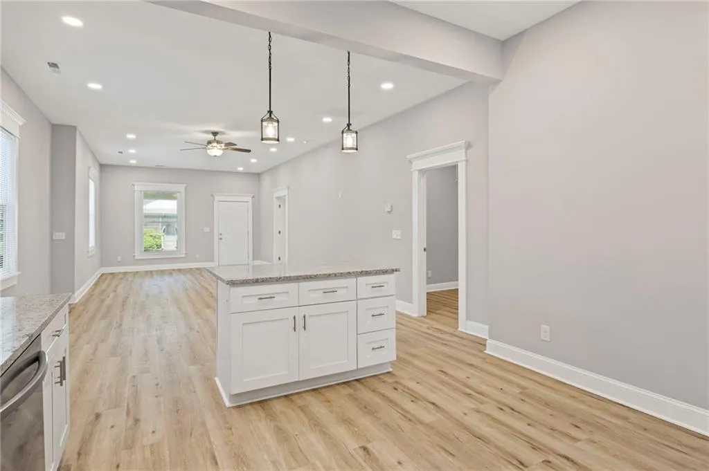 Kitchen with stainless steel dishwasher, light wood-type flooring, a ceiling fan, white cabinetry, and hanging light fixtures