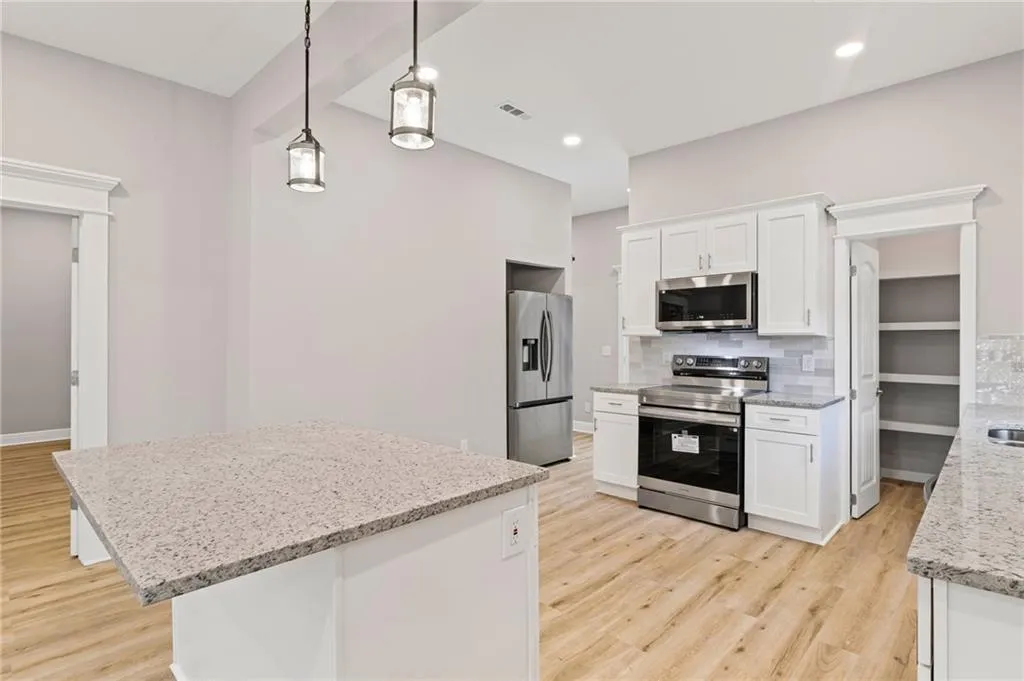 Kitchen with appliances with stainless steel finishes, light wood-style floors, decorative backsplash, white cabinetry, and hanging light fixtures