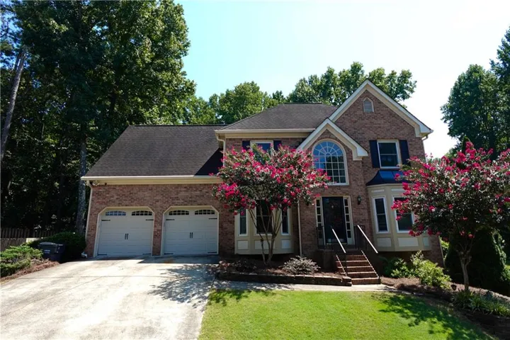 Brick exterior with a two-car garage, mature landscaping, arched window, and bay window
