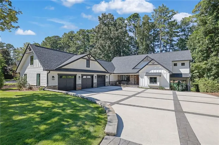 White board and batten siding, stone facade accents, dark asphalt shingle roof, three-car garage, and a large patterned concrete driveway