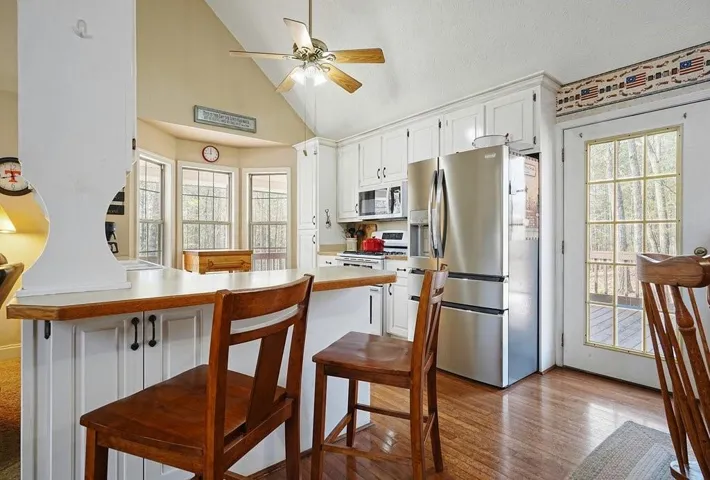 Kitchen with white appliances, a breakfast bar, light countertops, white cabinets, and vaulted ceiling