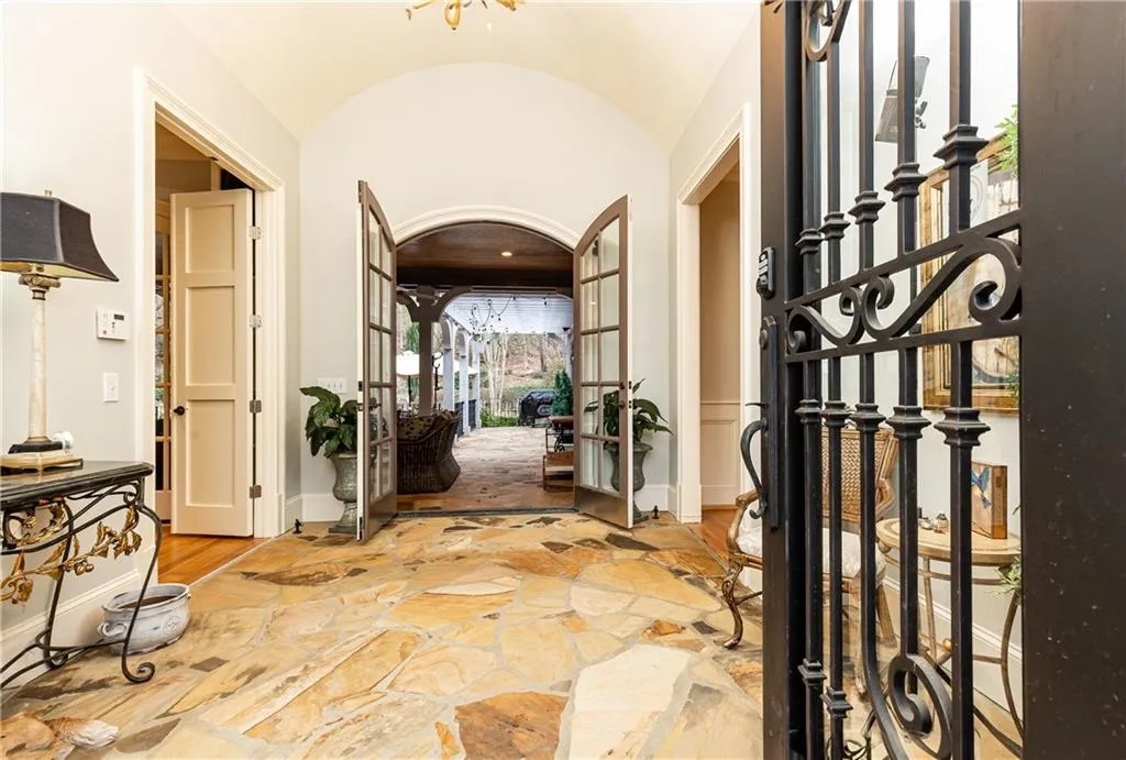 Substantial double iron doors open to Main Foyer with vaulted ceiling and flagstone floor. Straight ahead, French doors access Covered Back Patio and Backyard.
