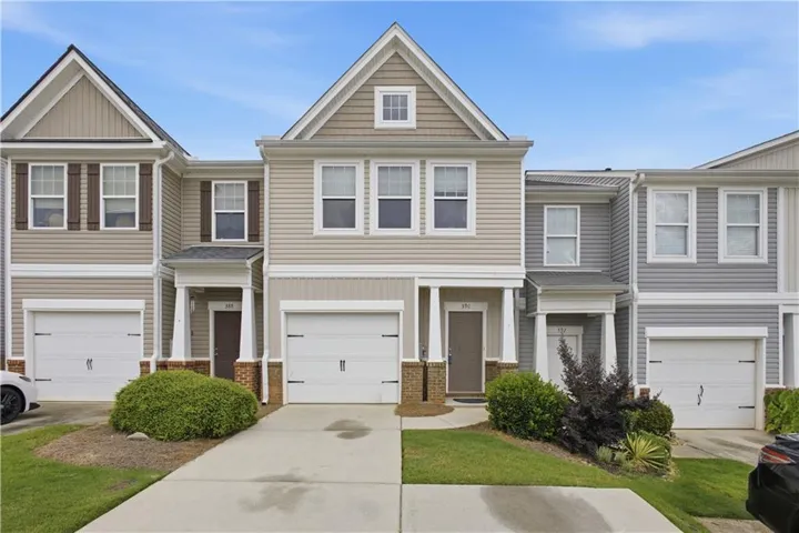 Townhouse exterior featuring siding, an attached garage, a covered entry, decorative shutters, and mature landscaping