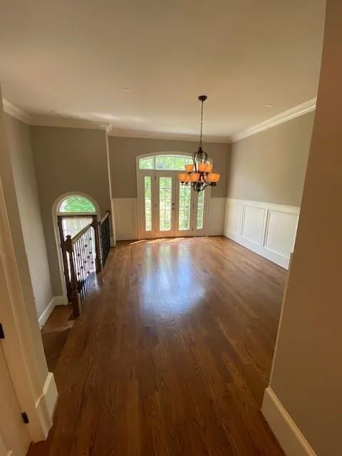 Unfurnished living room with ornamental molding, wood finished floors, a chandelier, a wainscoted wall, and a decorative wall