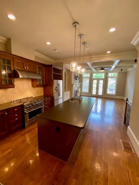 Kitchen with crown molding, hanging light fixtures, appliances with stainless steel finishes, decorative backsplash, and glass insert cabinets