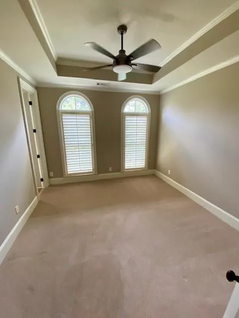 Empty room featuring a raised ceiling, ornamental molding, light carpet, and ceiling fan