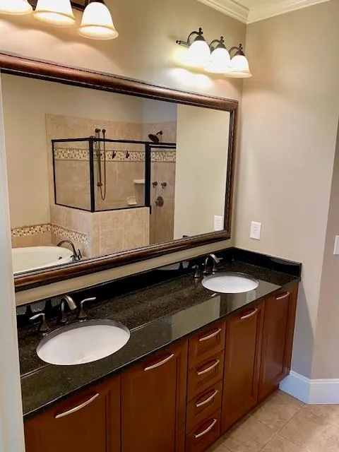Full bath with double vanity, a shower stall, ornamental molding, light tile patterned floors, and a garden tub