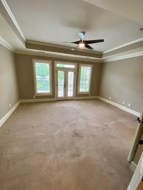 Unfurnished room with a raised ceiling, crown molding, carpet flooring, a ceiling fan, and french doors
