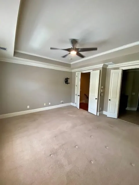 Unfurnished bedroom featuring a tray ceiling, light carpet, crown molding, ceiling fan, and a closet