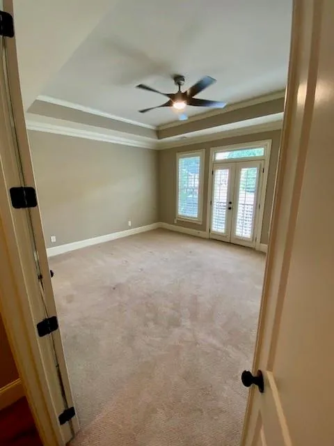 Unfurnished room with crown molding, a raised ceiling, light colored carpet, french doors, and a ceiling fan