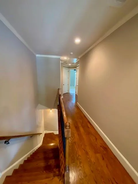 Hallway with an upstairs landing, dark wood-style floors, ornamental molding, and recessed lighting