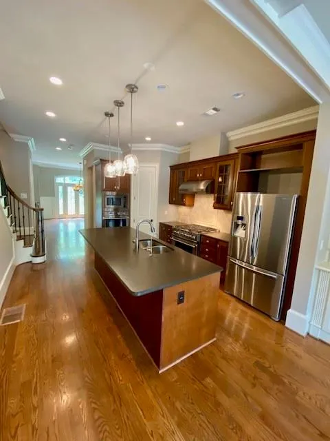 Kitchen featuring crown molding, appliances with stainless steel finishes, tasteful backsplash, an island with sink, and glass insert cabinets