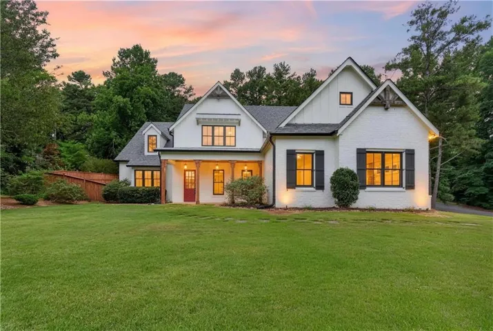White brick residence featuring a dark shingle roof, black window frames with shutters, a covered porch with natural wood columns, and a red entry door