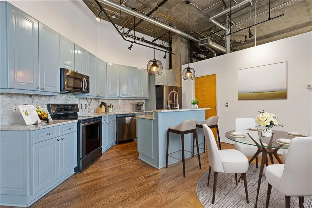 Kitchen with stainless steel appliances, a kitchen island with sink, dark wood-type flooring, a kitchen breakfast bar, and decorative light fixtures