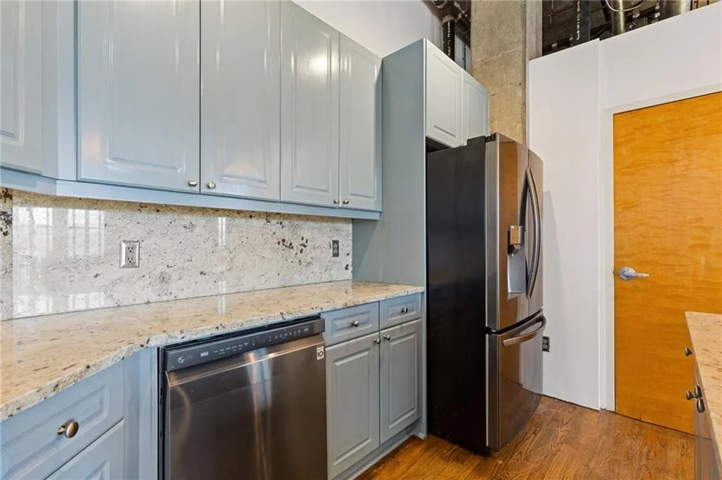 Kitchen featuring stainless steel appliances, gray cabinets, light stone counters, dark wood-type flooring, and decorative backsplash