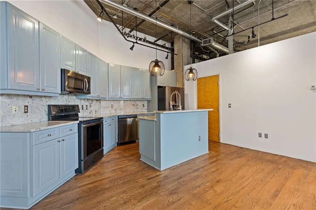 Kitchen with stainless steel appliances, a high ceiling, an island with sink, backsplash, and dark wood-type flooring