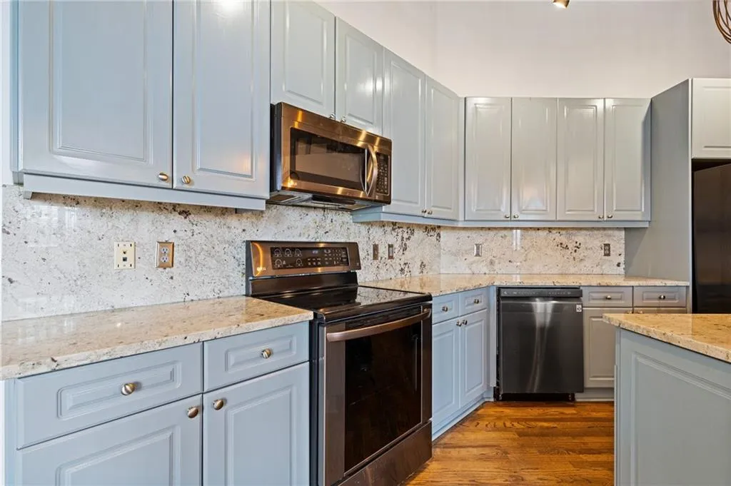 Kitchen featuring stainless steel appliances, gray cabinets, dark wood-style flooring, backsplash, and light stone counters