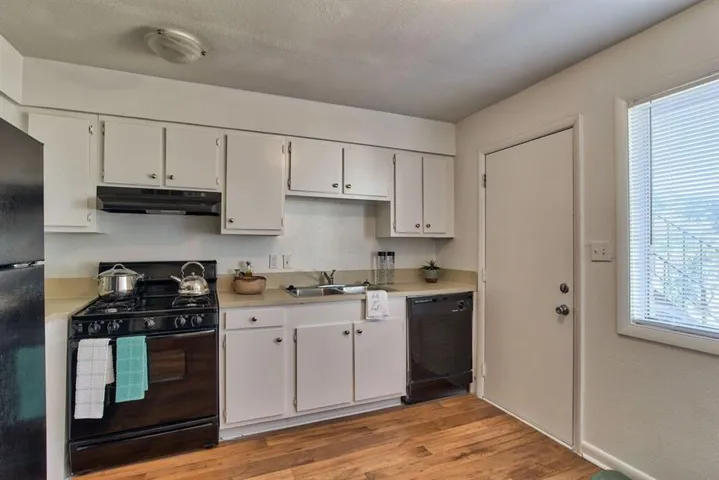 Kitchen featuring white cabinetry, a healthy amount of sunlight, black appliances, and light hardwood / wood-style flooring