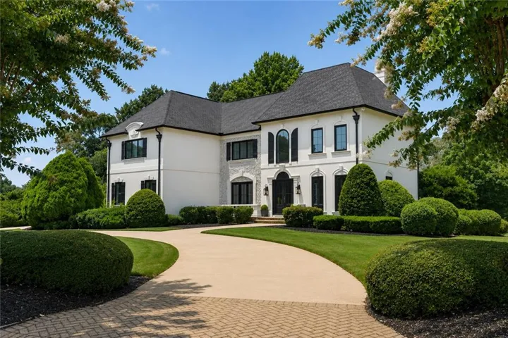 Stucco exterior with stone veneer accents, arched entryways, and a dark shingle roof