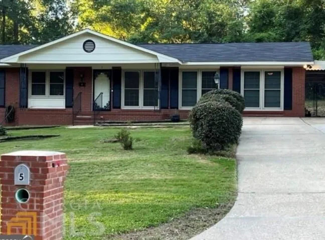 Brick ranch home featuring a gabled roofline, expansive front-facing windows, and a concrete driveway