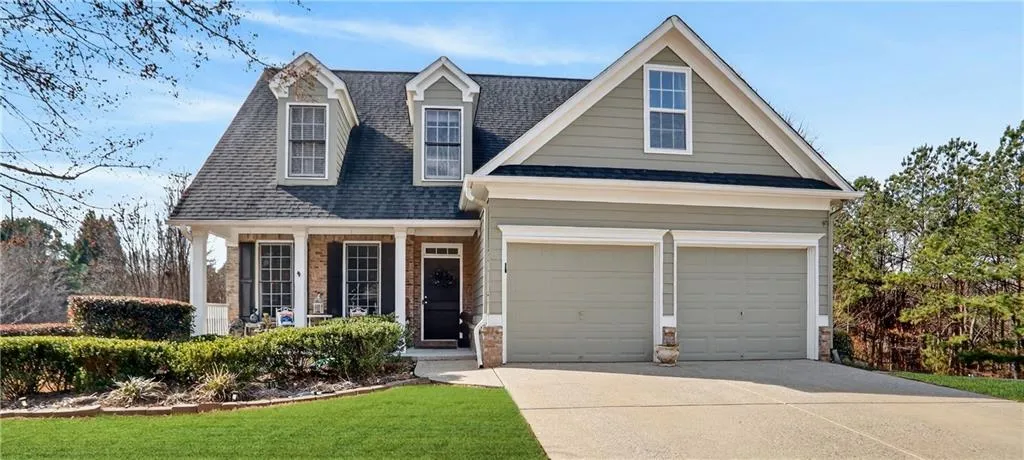 Two-story residence featuring dormer windows, a covered front porch, and a two-car garage with an expansive concrete driveway