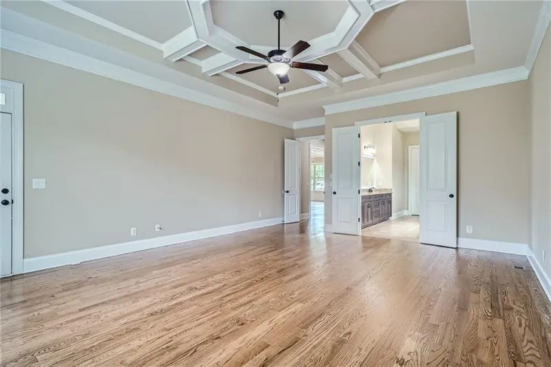 Unfurnished bedroom with coffered ceiling, light wood-style flooring, connected bathroom, crown molding, and beamed ceiling