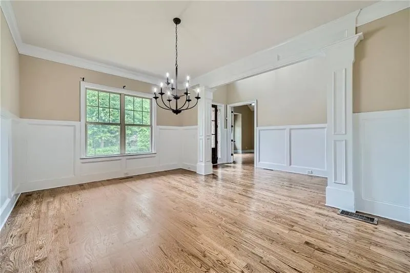 Unfurnished dining area featuring a decorative wall, a wainscoted wall, decorative columns, light wood-style floors, and ornamental molding