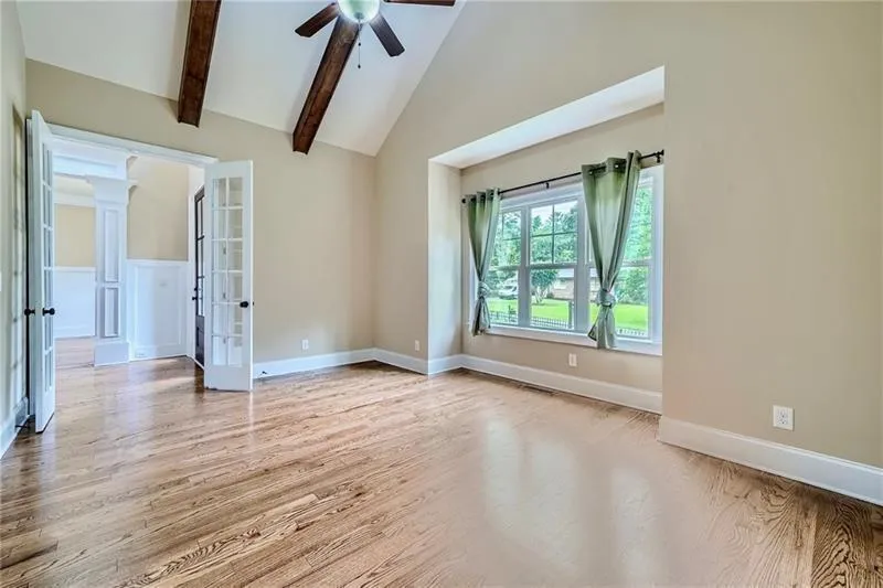 Unfurnished room with light wood-style flooring, decorative columns, high vaulted ceiling, beam ceiling, and a ceiling fan