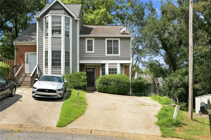 Two-story facade with gray siding and bay window, brick accent paneling, and a dark entry door