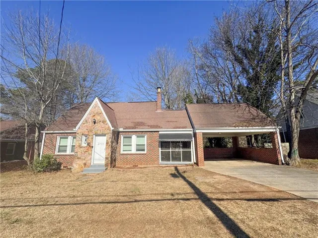 View of front of house with an attached carport, driveway, brick siding, a chimney, and a shingled roof