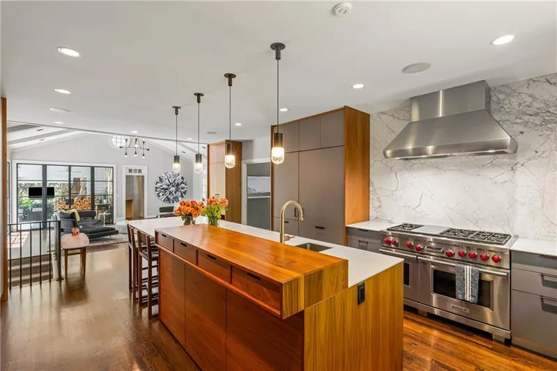 Kitchen with range with two ovens, wall chimney range hood, a sink, modern cabinets, and vaulted ceiling
