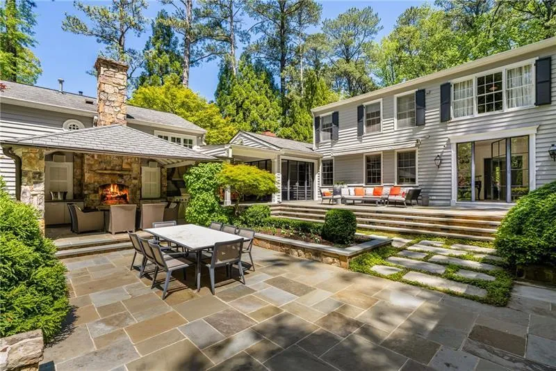Rear view of property featuring an outdoor living space with a fireplace, a patio, outdoor dining area, a chimney, and stone siding