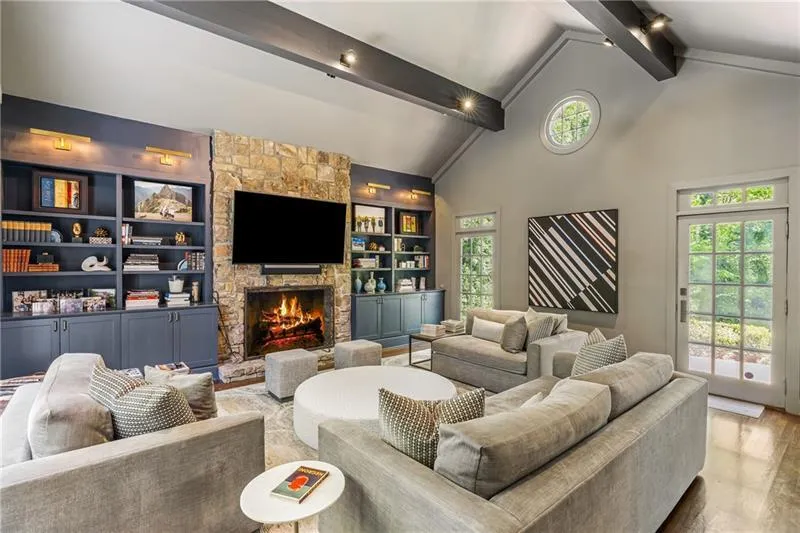 Living room featuring beam ceiling, a stone fireplace, wood finished floors, high vaulted ceiling, and built in shelves