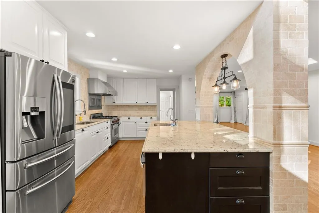 Kitchen featuring appliances with stainless steel finishes, white cabinetry, backsplash, light stone countertops, and light wood-style floors